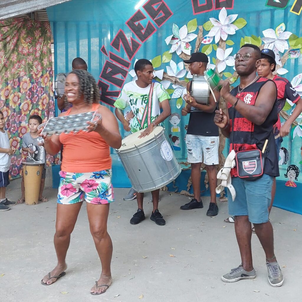 Pessoas com instrumentos musicais em frente ao cartaz do evento