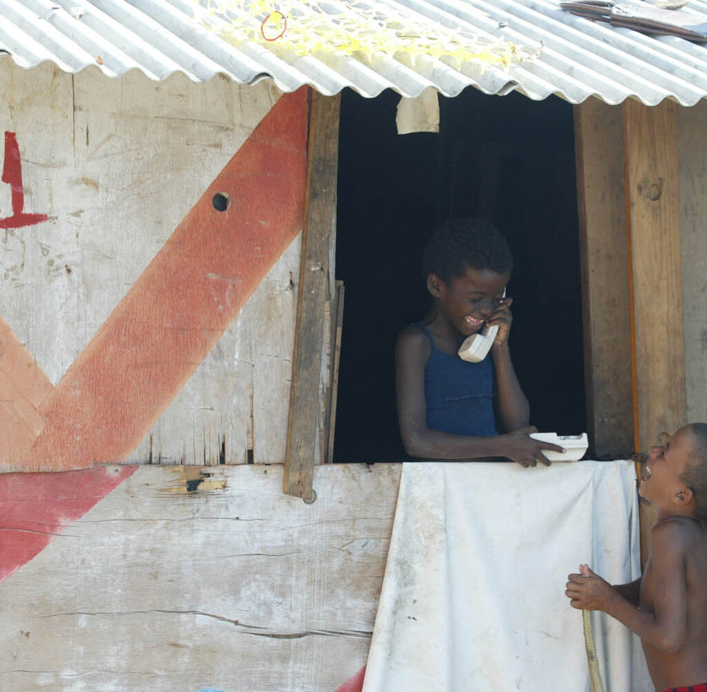 Crianças sorriem em moradia de madeira de aparência frágil