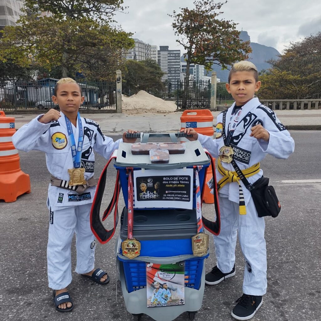 Dois pequenos atletas posam uniformizados ao lado da banquinha com bolo de pote